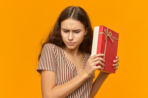 Curious cute girl in nice striped dress holding box with golden ribbon