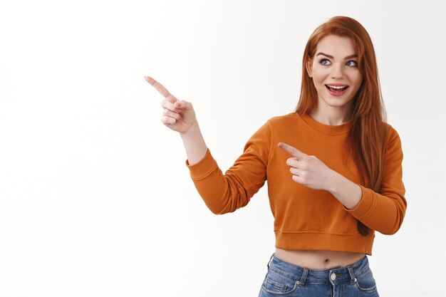 Curious enthusiastic good-looking redhead european female excited smiling broadly look pointing intrigued left side copy space interested awesome brand new product advertising, white wall