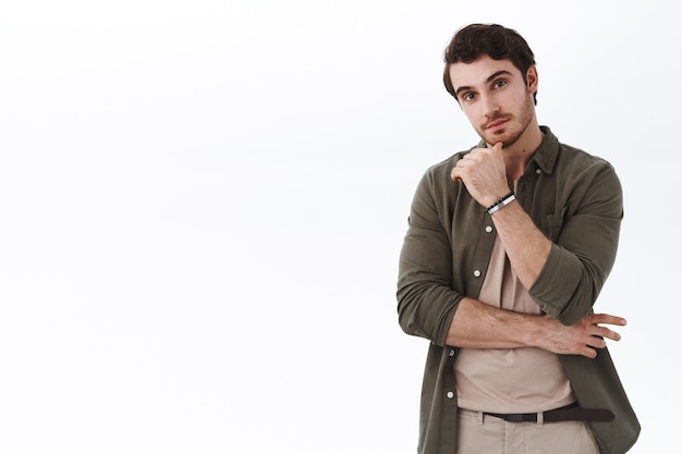 Curious and enthusiastic young caucasian bearded man standing near empty white copy space