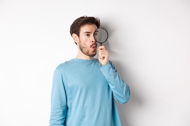 Curious guy looking through magnifying glass on right logo, saying wow, found cool thing, standing on white background