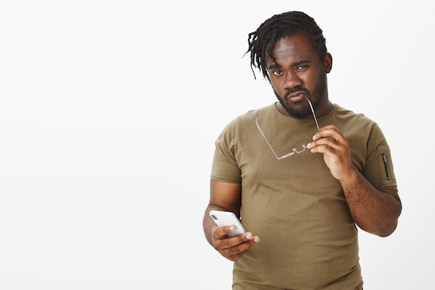 curious guy with glasses posing against the white wall with his phone