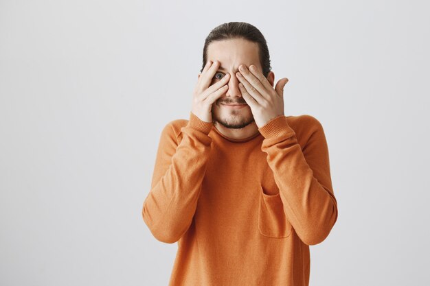 Curious hipster guy close eyes and peek through fingers interested