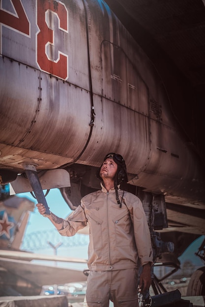 Curious pilot repairs vintage old  reactive fighter. He is wearing uniform and helmet.