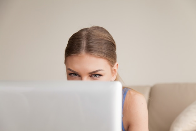 Любопытный подросток с помощью компьютера, молодая забавная девушка заглядывает за ноутбук