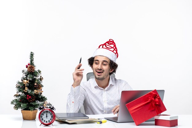 재미있는 산타 클로스 모자 쓰기 노트를 확인 하 고 흰색 바탕에 사무실에서 크리스마스를 축 하하는 호기심 젊은 사업가