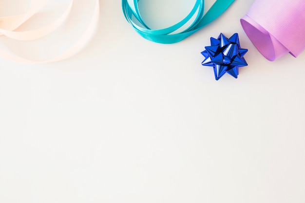 Curled colorful ribbon and blue stain bow on white background