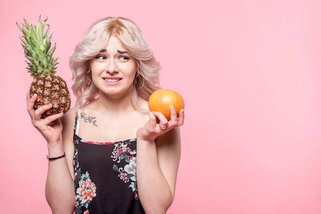 Free photo curly beautiful woman making choice between pineapple and orange in hands