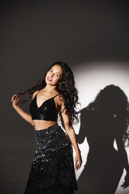 Curly brunette girl sitting near big disco ball and posing for a photo Girl wearing velour bodysuit Projectors light girl up