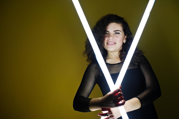 Free photo curly brunette plus size model with two long led lamp against yellow wall