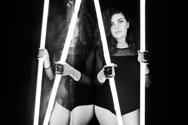 Curly brunette plus size model with two long led lamp at dance room with mirror