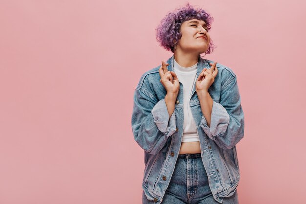 Curly charming woman in good mood and in bright clothes smiling. Cute adult woman in short top rejoices at something on pink.