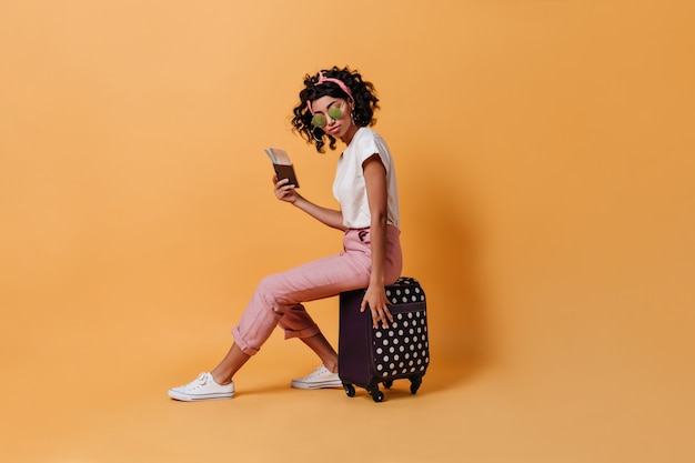 Curly female traveler sitting on suitcase