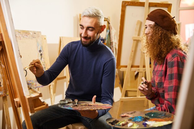 Кудрявая девушка и мужчина рисуют картину и улыбаются