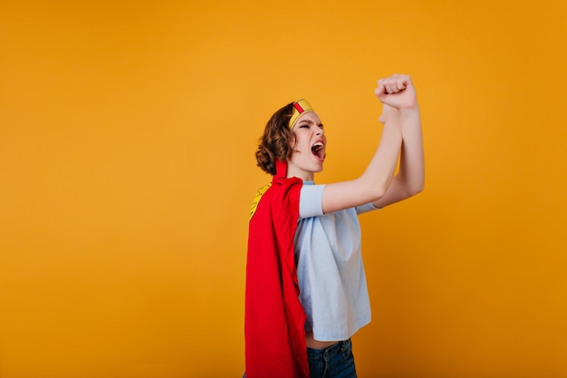 Curly girl in red cloak screaming on yellow space