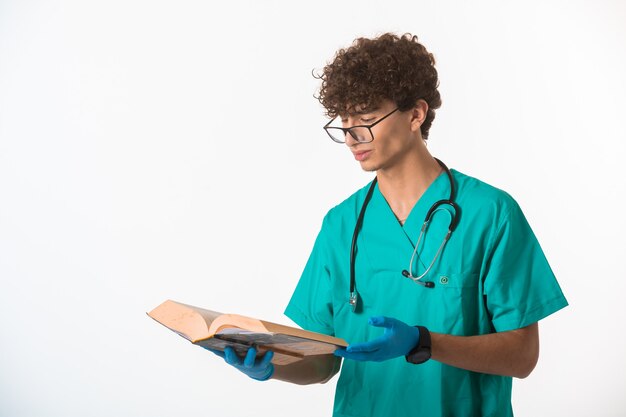 Curly hair boy in medical uniform and hand masks attentively reading.
