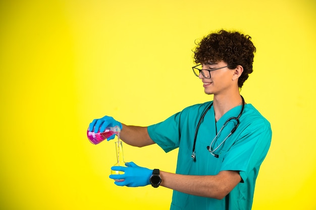 Curly hair boy in medical uniform and hand masks doing reaction with chemical liquid in happy manner