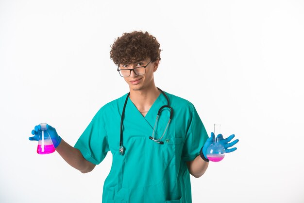 Curly hair boy in medical uniform and hand masks doing test in chemical flasks.