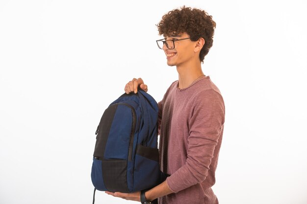 Curly hair boy in optique glasses holding backpack, looking aside and smiling.