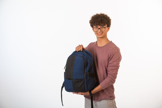 Curly hair boy in optique glasses holding backpack and smiling.