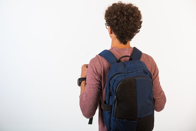 Curly hair boy in optique glasses holding his backpack .