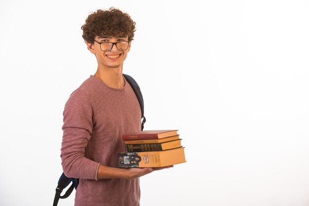 笑みを浮かべて、自信を持って見える学校の本を保持している光学メガネの巻き毛の少年。