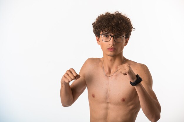 Curly hair boy in optique glasses punching with fists. 