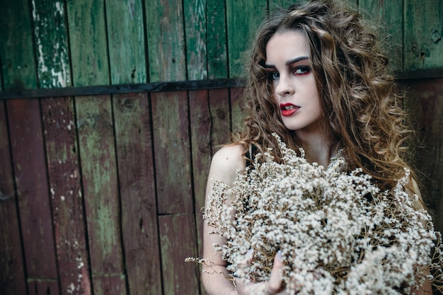 Ragazza dei capelli ricci posa su un muro sporco