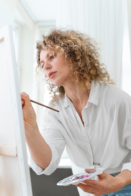 Curly-haired blonde woman painting at home