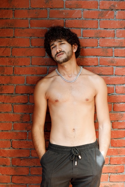 Free photo curly haired half naked man posing to camera against wall.