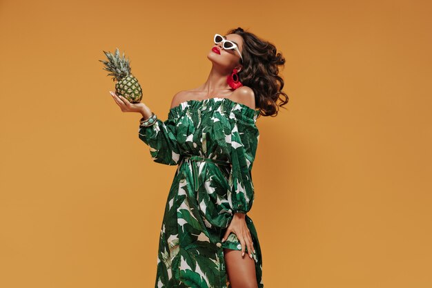 Curly haired modern girl with red bright big lips and unusual earrings in stylish green and white sundress and sunglasses