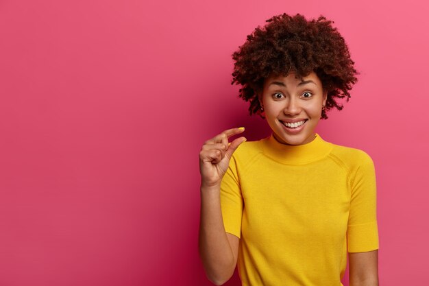 Curly haired positive woman measures tiny object, shows something very little