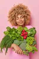 Free photo curly haired woman carries different green vegetables bought at market keeps eyes closed going to enrich with vitamins keeps eyes closed isolated over pink background healthy nutrition concept