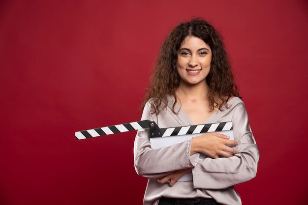Curly haired woman with clapperboard standing.