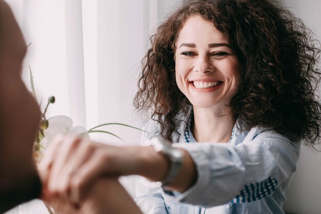 Curly lady reaches out her hand to the man sitting before bright window in the morning