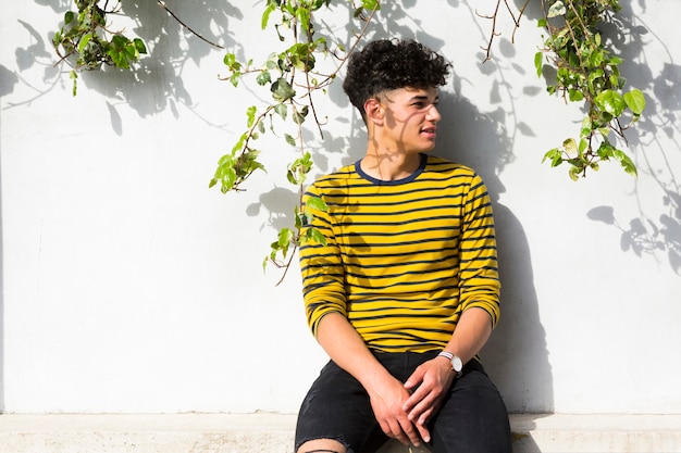 Free photo curly man in striped shirt sitting and looking away