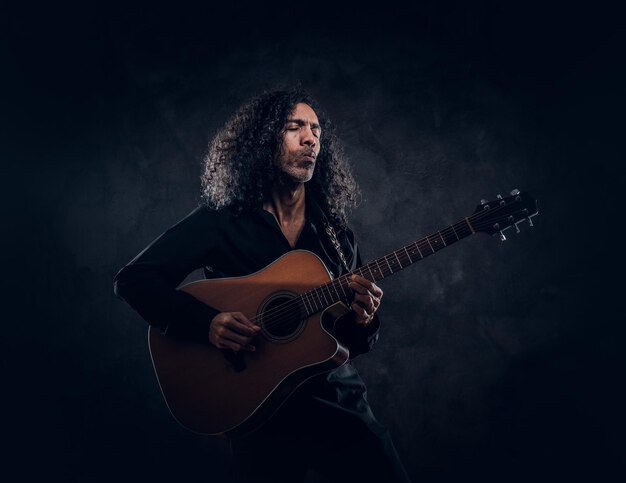 ギターを持ったカーリーマンがスタジオで彼の新しいアコースティックの傑作を発表しています。