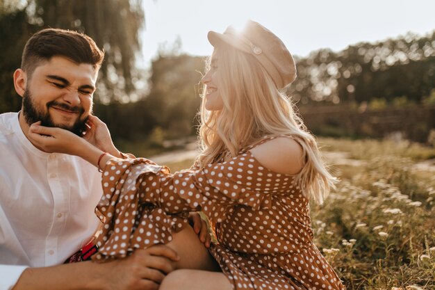 Curly mischievous girl tickles her bearded husband. Sunny portrait of happy family couple in park.