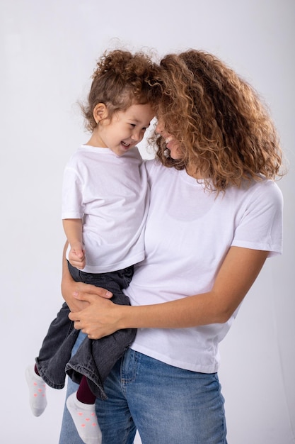 Foto gratuita madre e figlia ricci che posano su uno sfondo bianco con magliette bianche