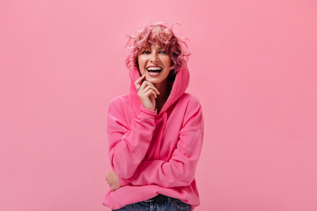 Foto gratuita la donna dai capelli rosa riccia di buon umore posa sul muro isolato