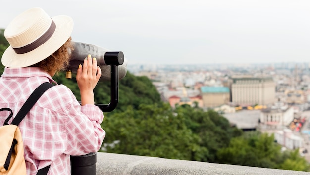 Curly woman looking at the town through a telescope with copy space