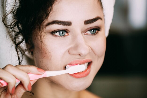 Curly woman with blue eyes cleans her teeth