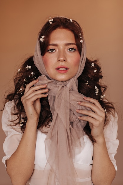 Free photo curly woman with flowers in her hair tying scarf in bow and looking at camera.