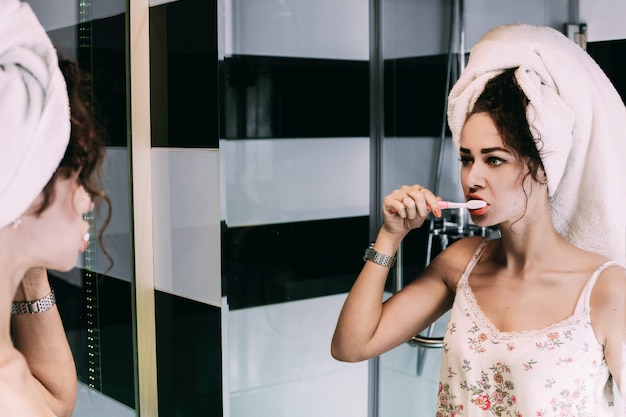 Curly woman with towel on her head cleans her teeth