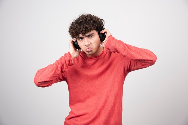 Curly young man with headphones listening song with bored expression.