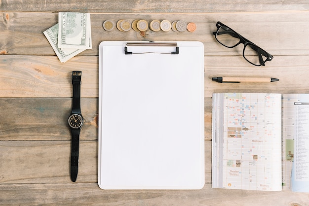 Currency notes and coins with wristwatch; eyeglasses; pen; diary and paper on clipboard over wooden table