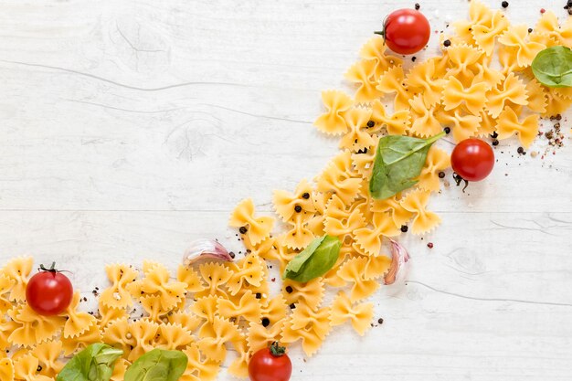 Curved shape made with farfalle pasta and tomato; garlic clove; basil leaf on wooden background