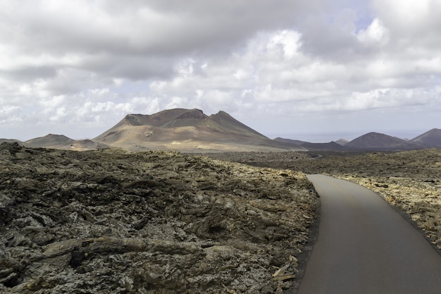 Curvy road surrounded by hills under a cloudy sky in Timanfaya National Park in Spain