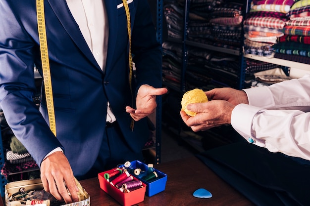 La mano del cliente che mostra la palla gialla della lana allo stilista maschio in negozio