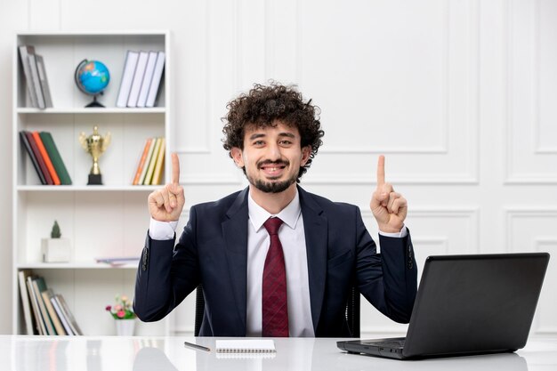 Customer service curly brunette young man in office suit and red tie with laptop excited