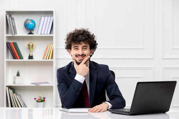 Customer service curly brunette young man in office suit and red tie with laptop smiling happily